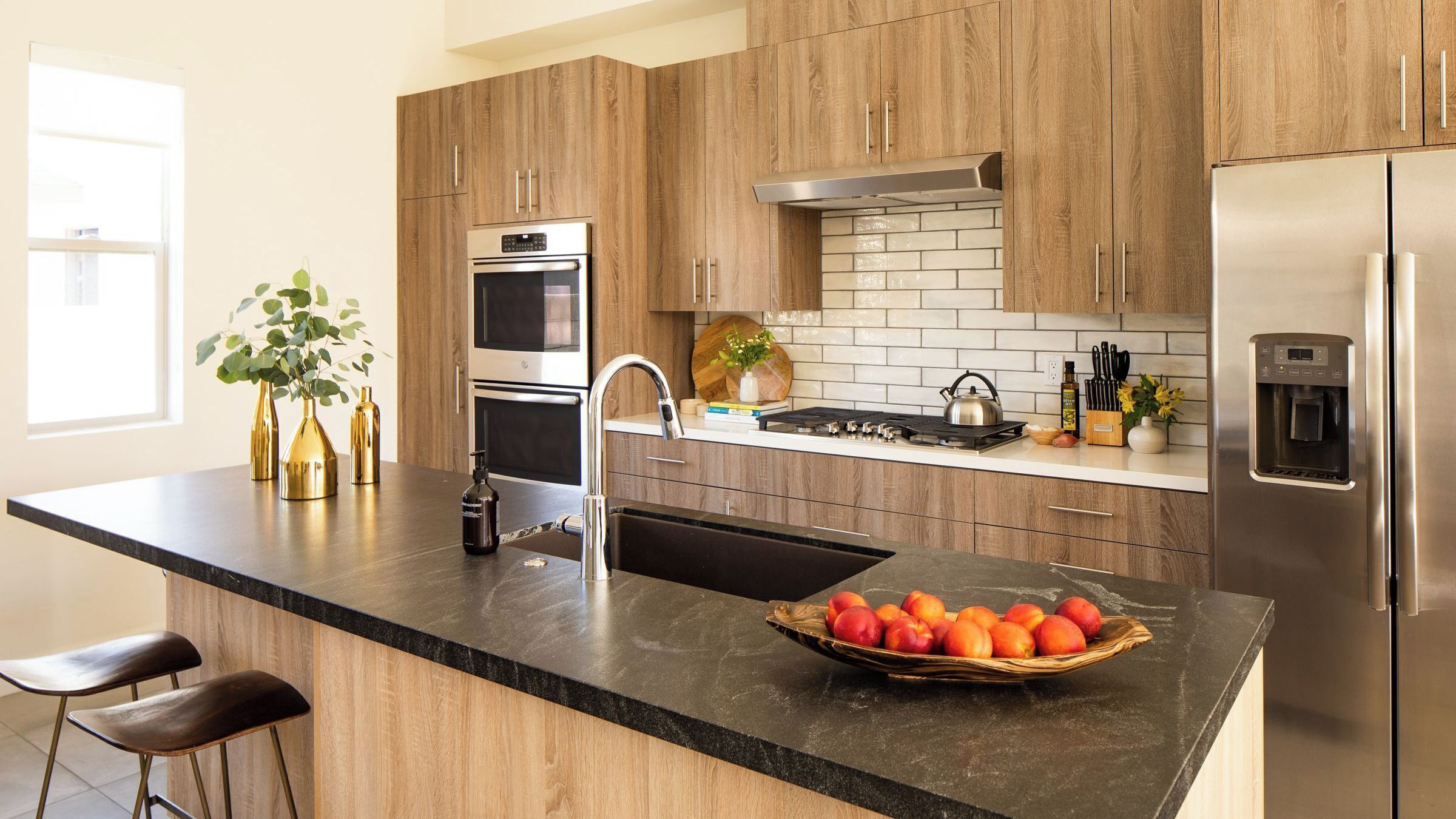 A modern kitchen with wooden cabinets, a stainless steel refrigerator, a built-in oven, and a granite countertop.