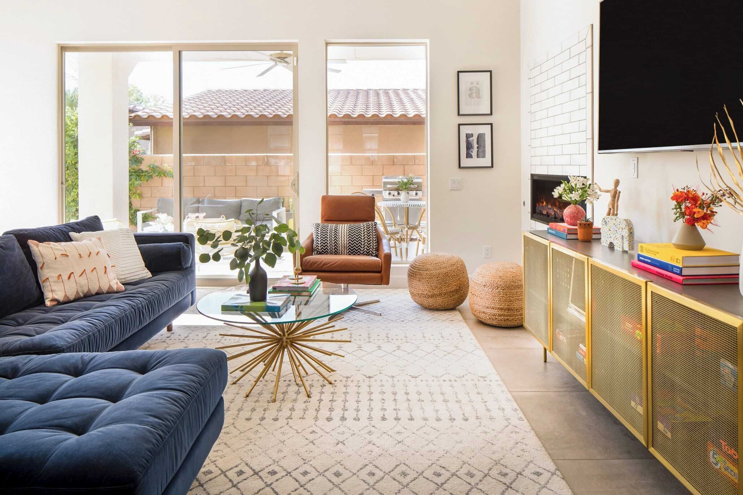 A modern living room with a blue sofa, a glass coffee table, a patterned rug, and a yellow cabinet.