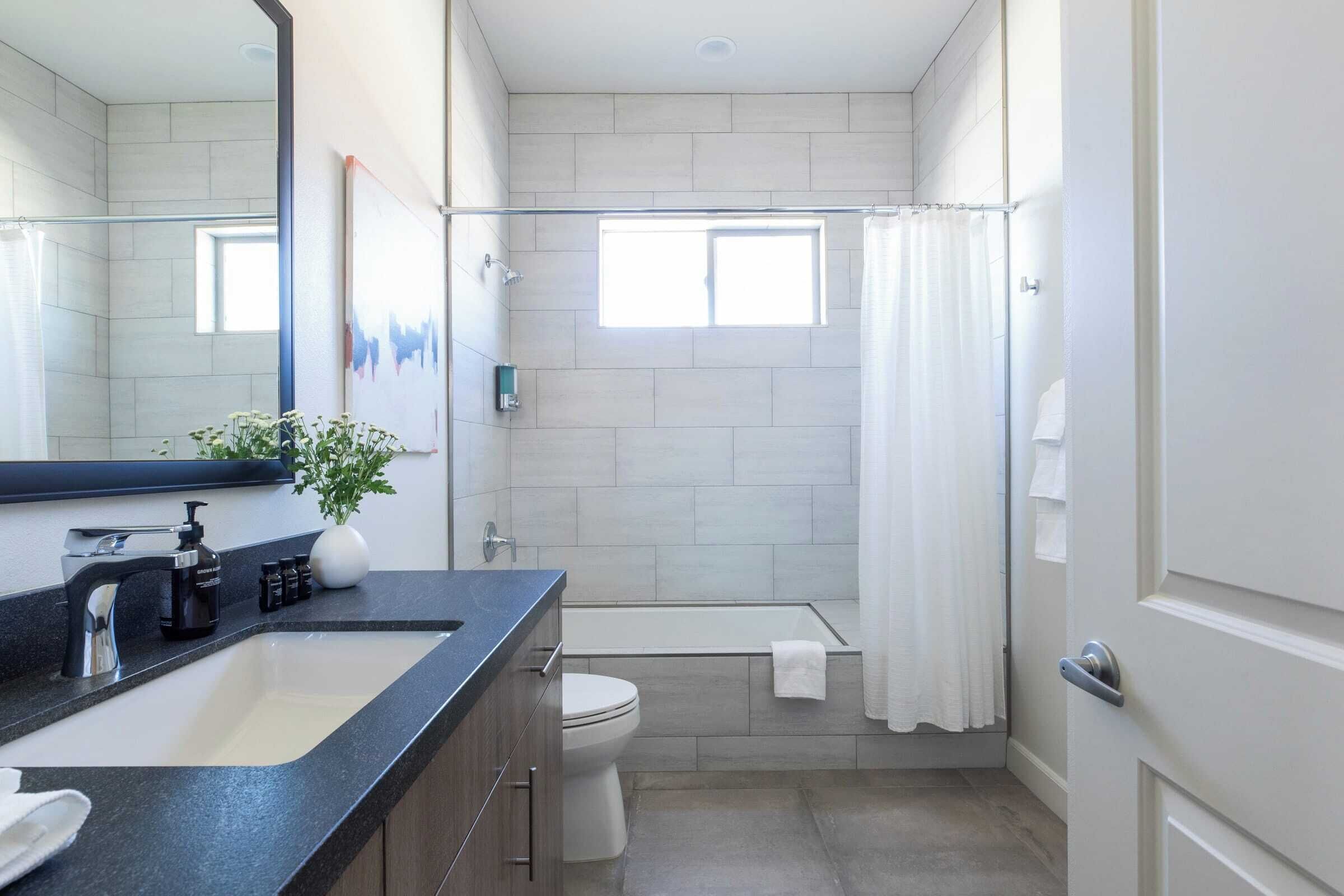 A modern bathroom with a large mirror, a sink, a toilet, and a shower area.