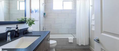 A modern bathroom with a large mirror, a sink, a toilet, and a shower area.