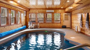 En stuga byggd av trä med en pool, stora fönster och en dörr.