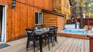 A wooden cabin with a deck, a hot tub, and a dining area with chairs and a table. - Walk to Ski Resort Lift Deck, Hot Tub, Game Loft Jumper by Avantstay (Big Bear Lake)