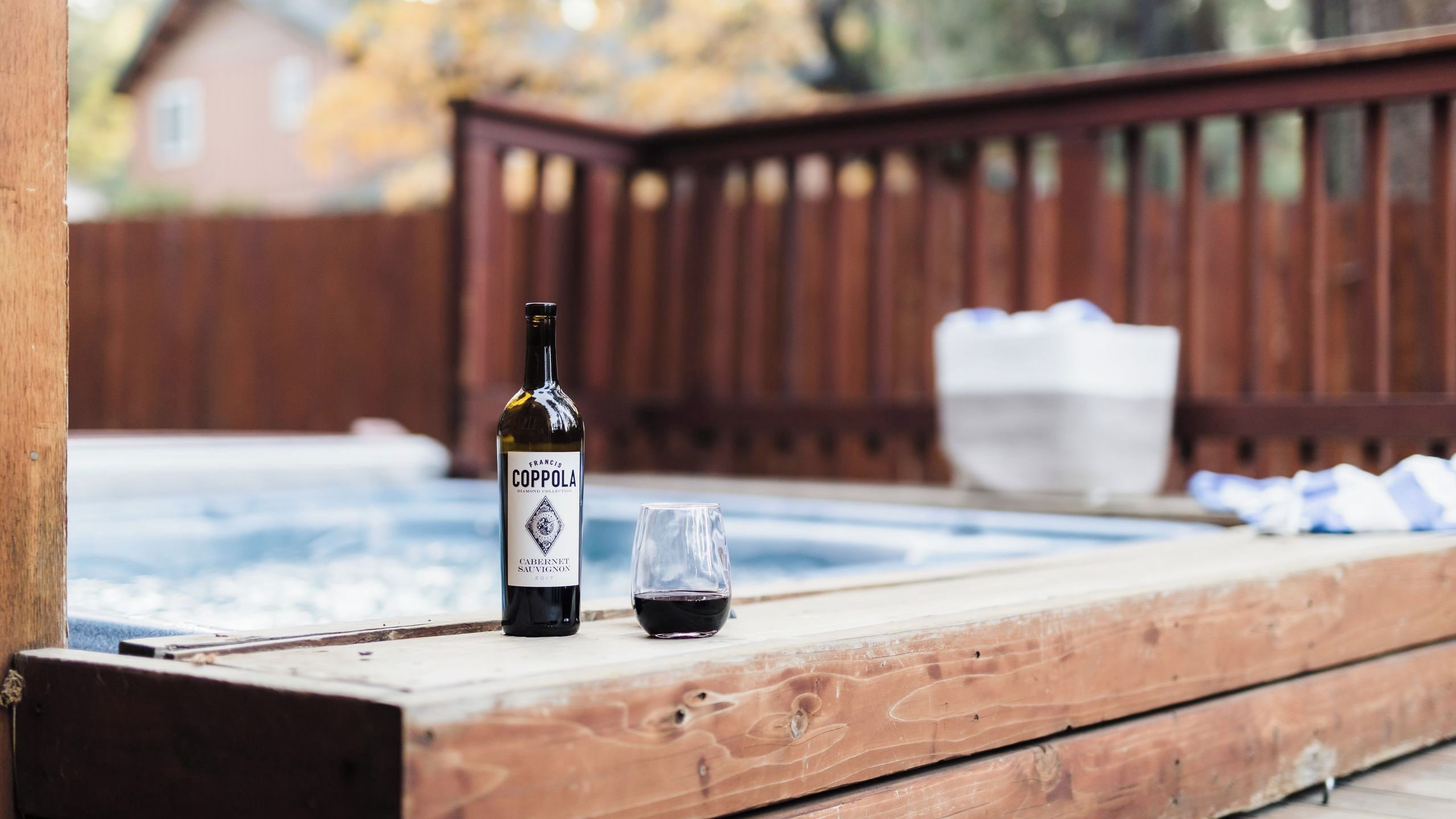 A wooden deck with a hot tub, a bottle of Francis Coppola Cabernet Sauvignon, and a glass of wine.