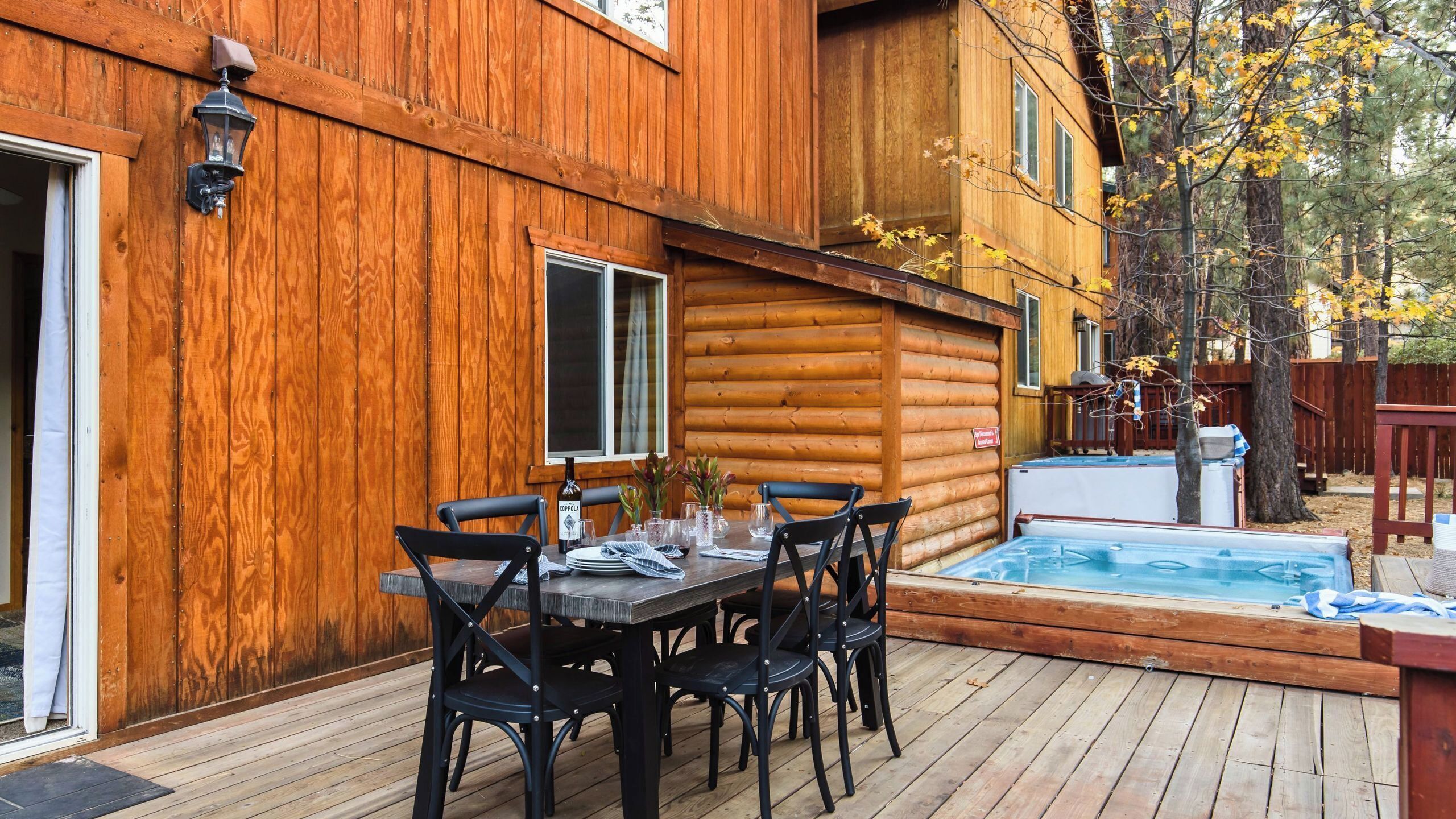 Una cabaña de madera con un patio, un jacuzzi y una mesa de comedor preparada para cuatro.