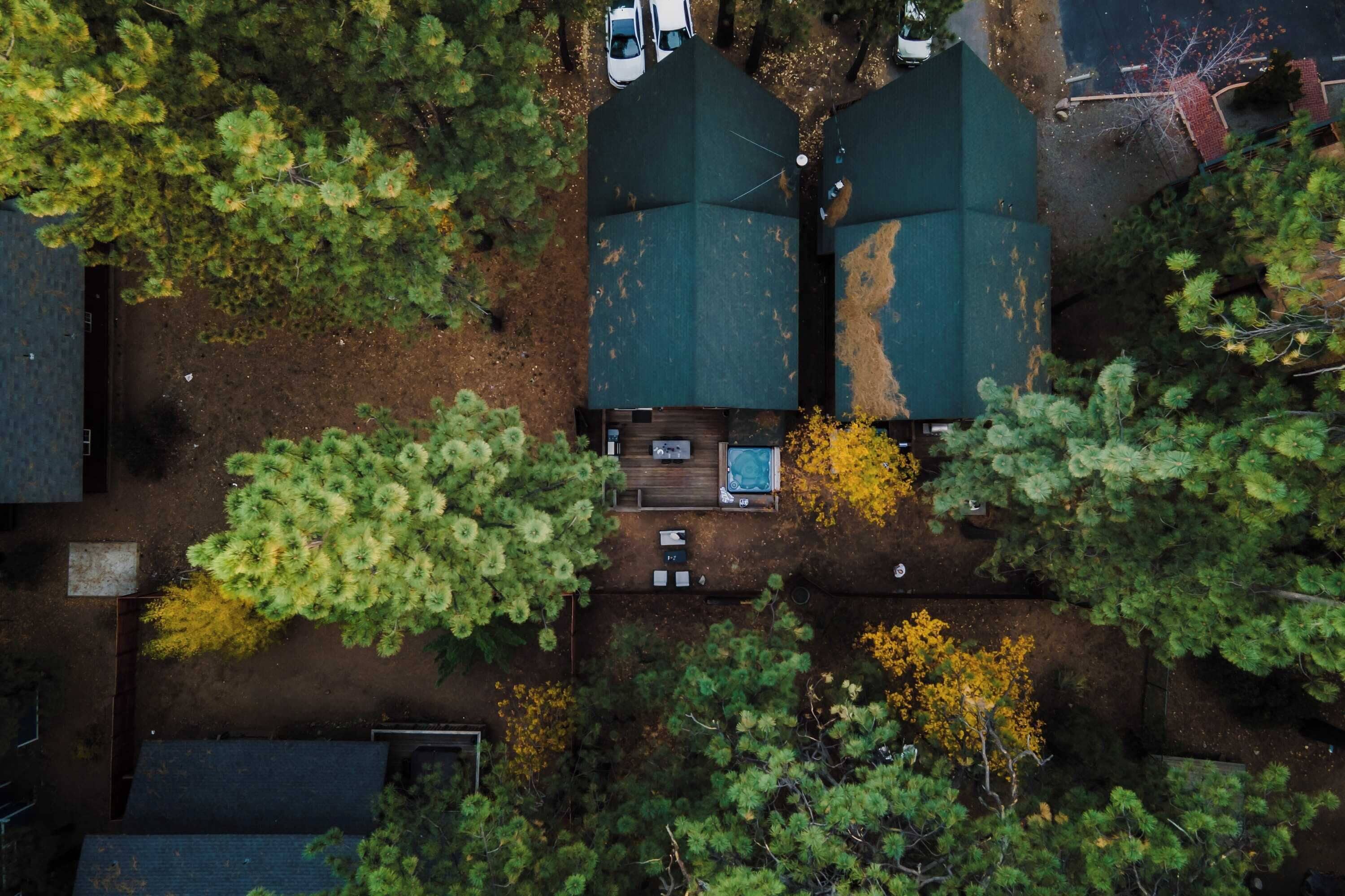 Vista aérea de una zona residencial con dos casas de techo verde, rodeadas de árboles y un pequeño camino de entrada.