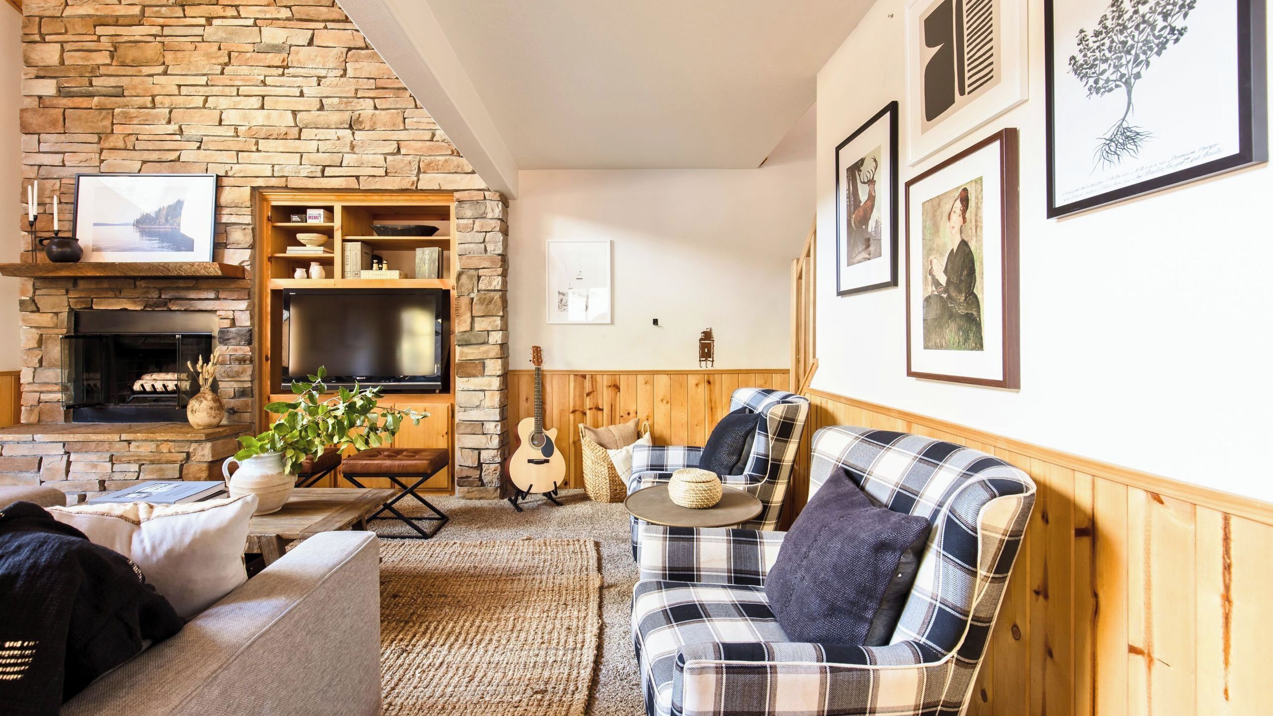 A cozy living room with a stone fireplace, a television, a guitar, and a plaid armchair.