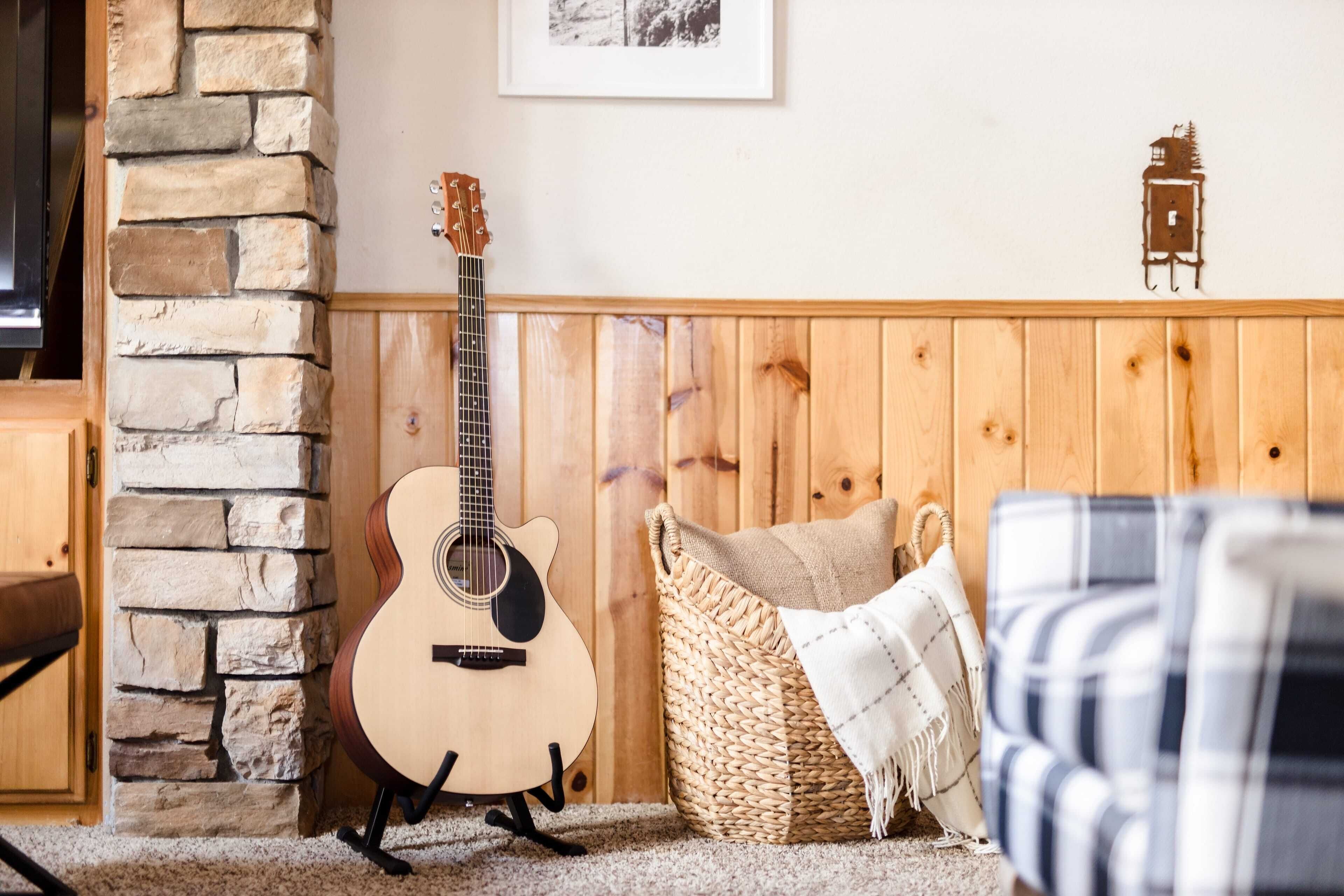 Una habitación acogedora con pared de piedra, un banco de madera, una cesta de mimbre y una guitarra.
