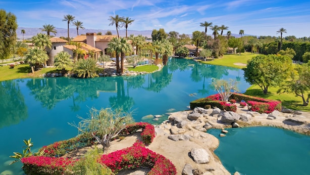 A resort with a large pool, palm trees, and a mountainous backdrop.