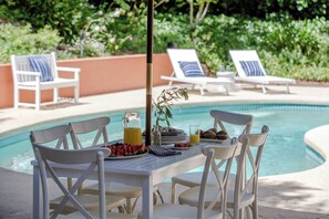 A poolside dining area with white chairs and a table set with breakfast items.