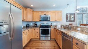 A modern kitchen with wooden cabinets, stainless steel appliances, granite countertops, and a large window providing natural light.