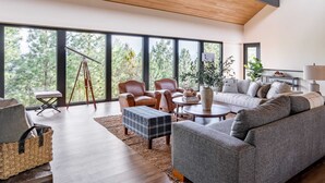A spacious living room with large windows, a wooden ceiling, and a modern sofa set.