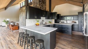 A modern kitchen with a large island, dark cabinets, and a stone accent wall.
