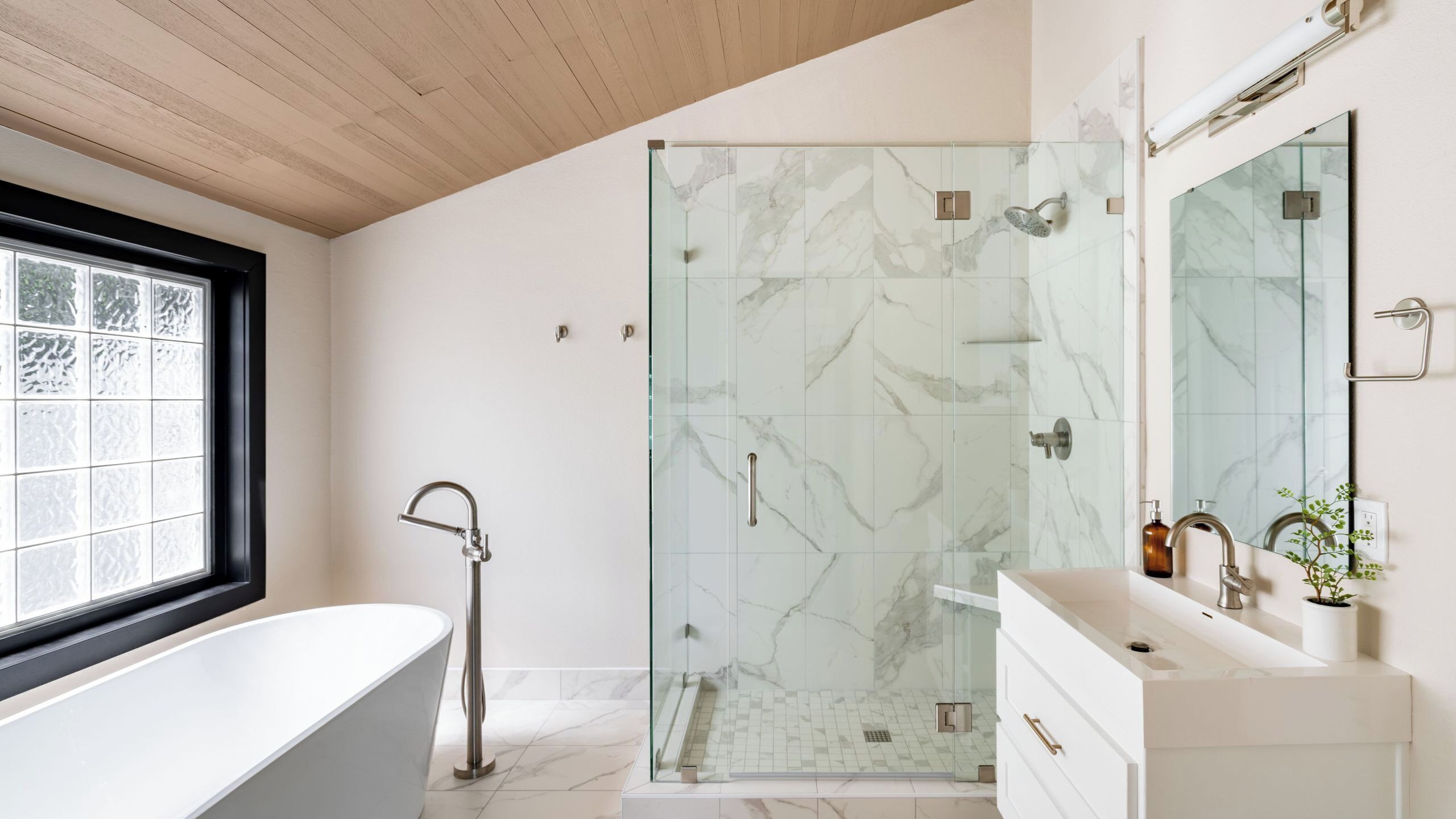 A modern bathroom with a glass-enclosed shower, a freestanding bathtub, and a vanity with a mirror.