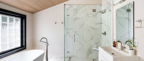 A modern bathroom with a glass-enclosed shower, a freestanding bathtub, and a vanity with a mirror.