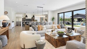 Un salon spacieux avec un grand canapé, une table basse et une vue sur la cuisine et l’espace extérieur.