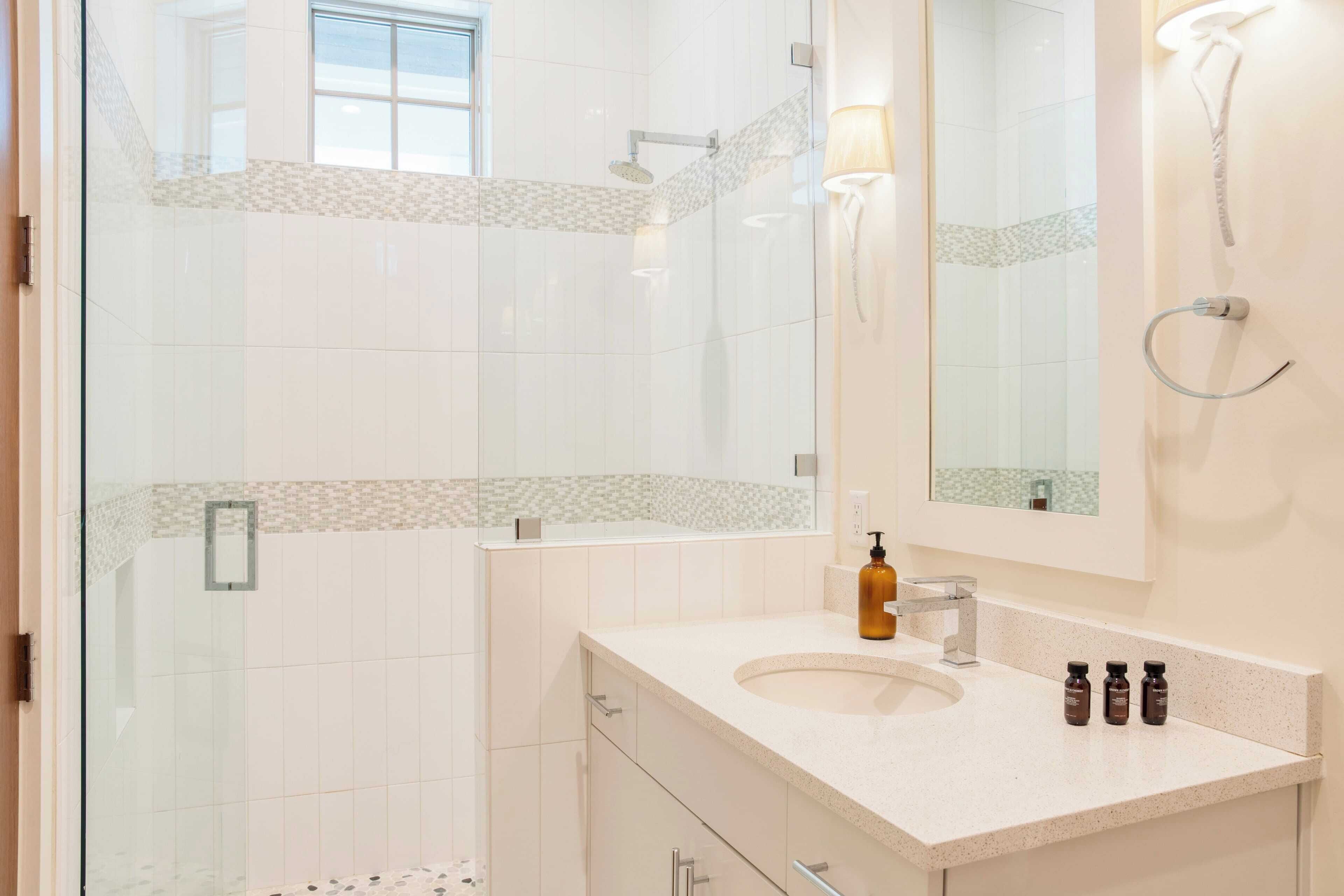 A modern bathroom with a glass-enclosed shower, a large mirror, and a countertop with toiletries.