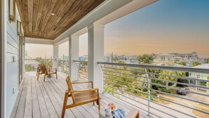 A covered balcony with wooden flooring, metal railings, and a view of a residential area. - Monarch by Avantstay Stunning Estate 1 Block to Beach, Swim Up Bar, Hot Tub, & Rooftop Views (Destin)