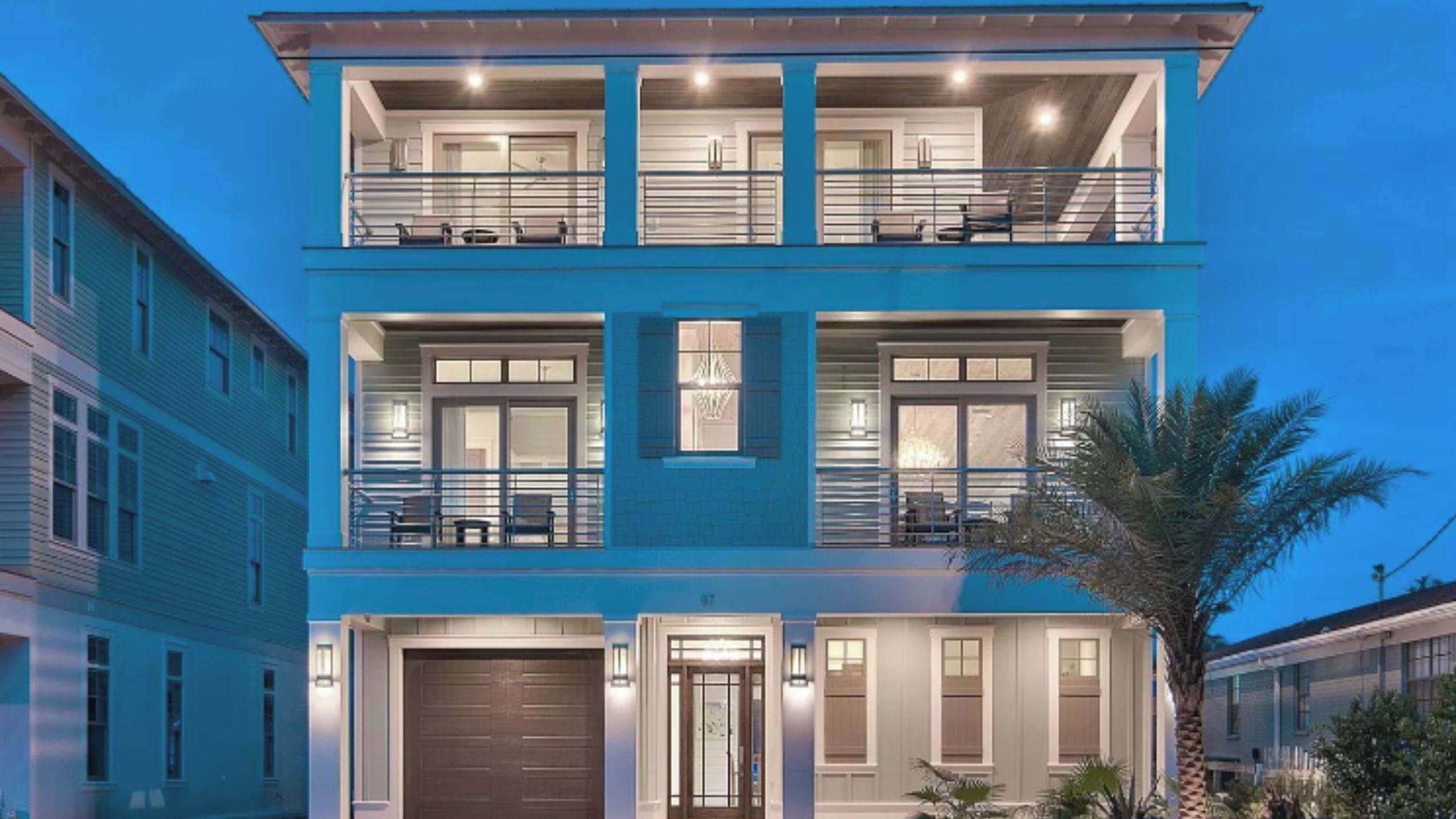 A two-story building with a balcony on the upper floor, a garage door, and a palm tree in the foreground.