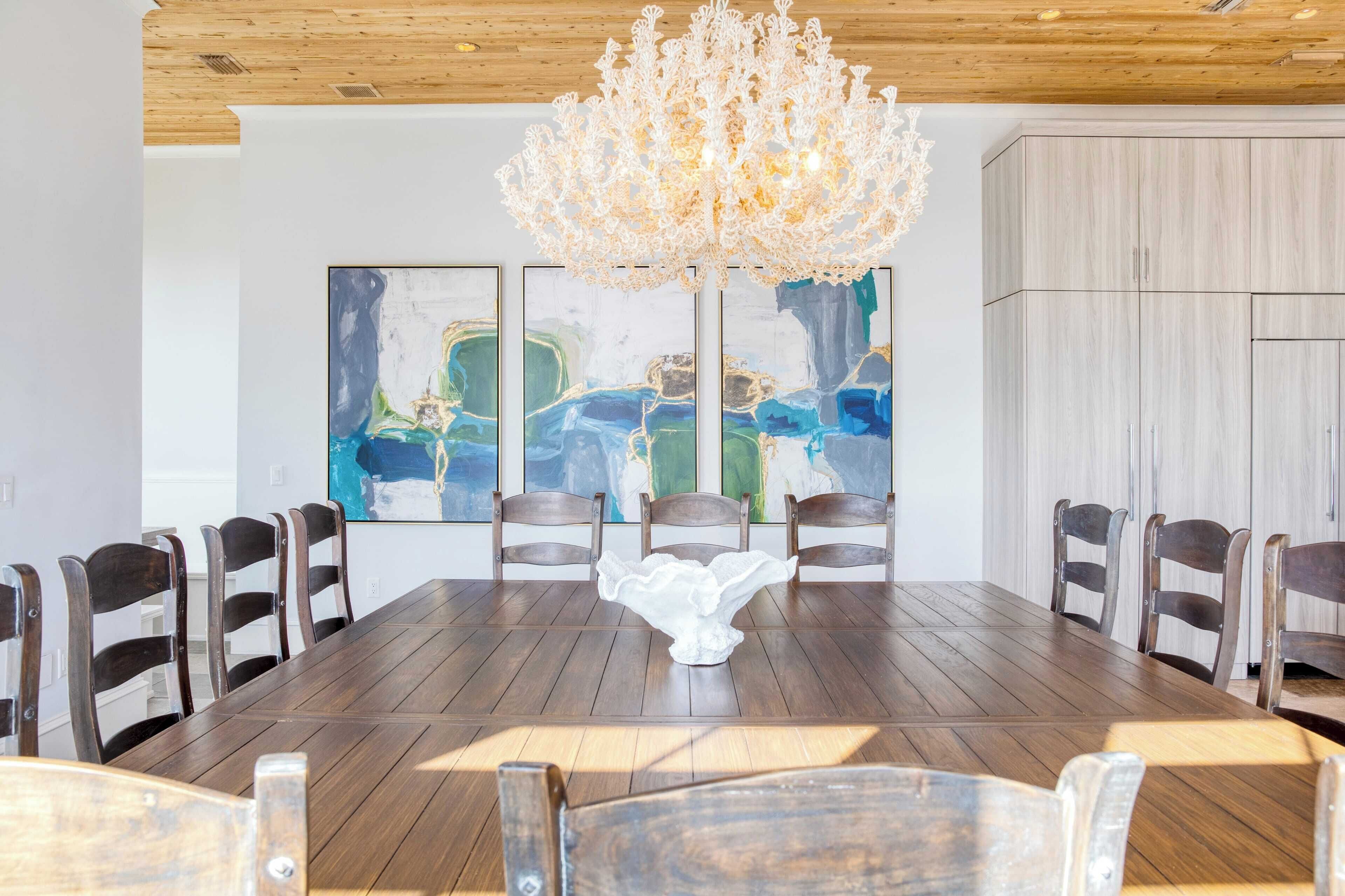 A dining area with a wooden table, six chairs, a chandelier, and abstract paintings on the wall.