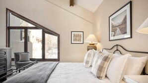 A bedroom with a large window, a bed with multiple pillows, a chair, a desk, and a lamp. - Cloud 9 by Avantstay Located at the Base of Vail Ski Resort w/ Community Pool & Hot Tub (Vail)