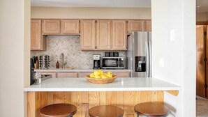 A modern kitchen with wooden cabinets, a stainless steel refrigerator, a coffee maker, and a bowl of lemons on the counter. - Cloud 9 by Avantstay Located at the Base of Vail Ski Resort w/ Community Pool & Hot Tub (Vail)