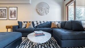 A living room with a sectional sofa, a coffee table, and a large window.