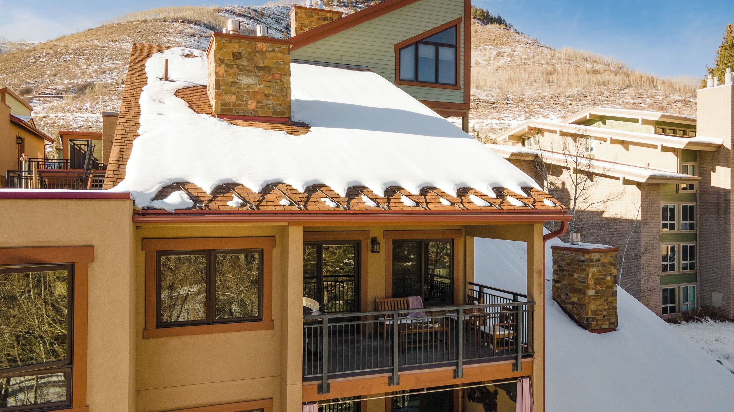 A building with a snow-covered roof, a balcony with a railing, and a mountainous backdrop.