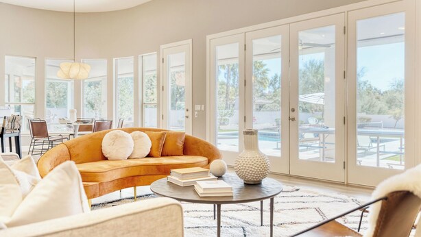 A spacious living room with a large sofa, a coffee table, and a dining area visible through the glass doors. - Sunridge by Avantstay Glorious Scottsdale Estate w/ Pool, Hot Tub, Ping Pong & Pool Table! (Scottsdale)