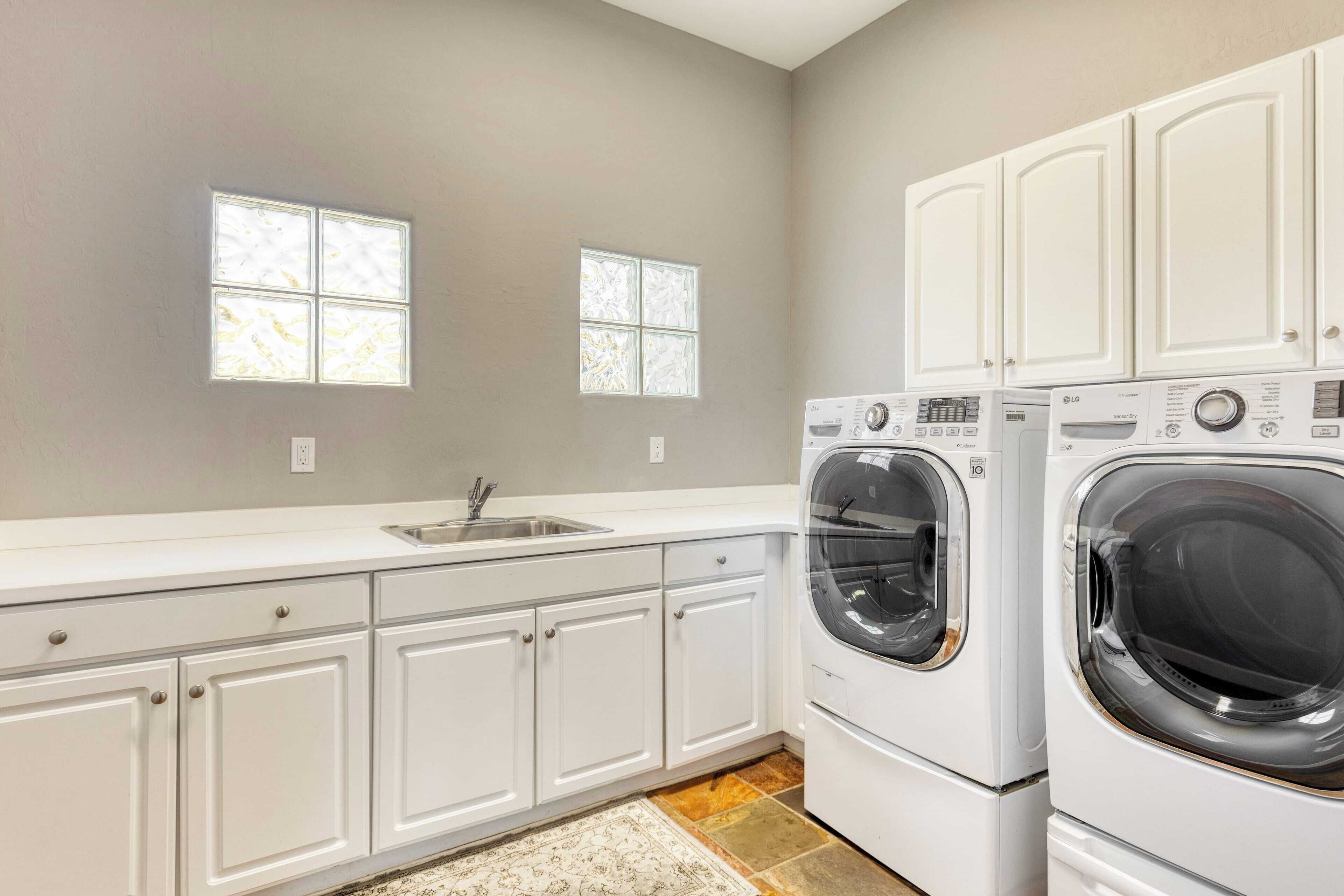 A laundry room with two stacked washers and dryers, a sink, and two windows.