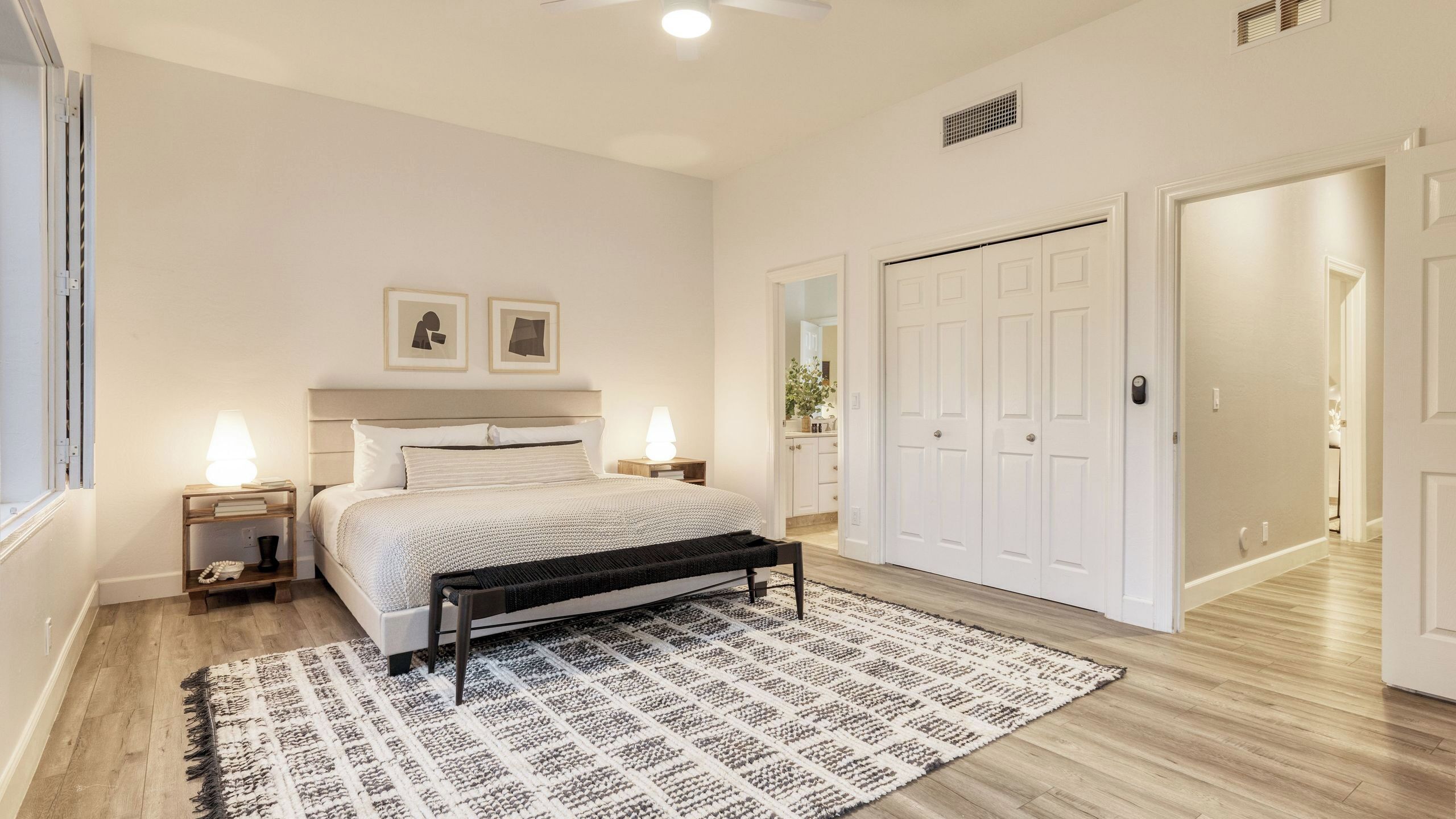 A bedroom with a bed, bedside lamps, a bench, a patterned rug, and a wardrobe.