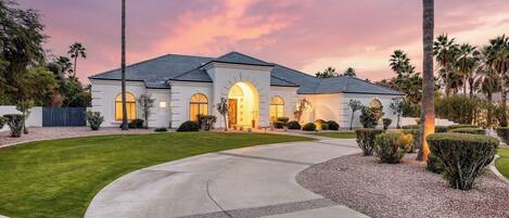 A two-story house with a curved driveway, arched windows, and a well-maintained lawn.