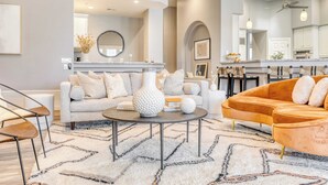 A modern living room with a sofa, armchair, coffee table, and a dining area with a kitchen in the background. - Sunridge by Avantstay Glorious Scottsdale Estate w/ Pool, Hot Tub, Ping Pong & Pool Table! (Scottsdale)