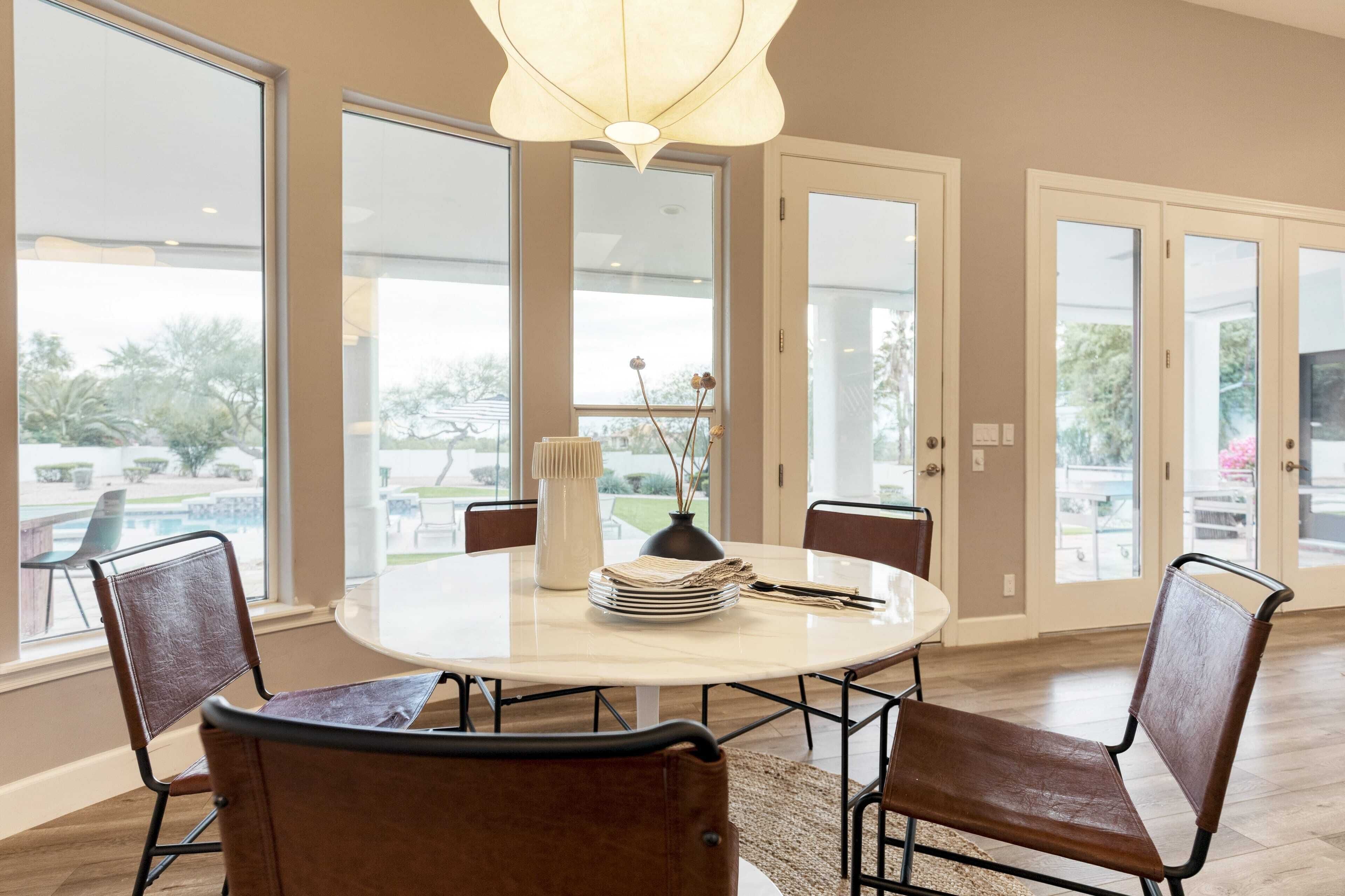 A dining area with a round table, four chairs, a vase with dried flowers, and a lamp.