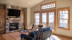 A living room with a stone fireplace, a flat-screen TV, a sofa, and large windows. - Lakefront Home in Kings Beach w/ Views Prime Location Atkinson by Avantstay (Kings Beach)