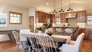 A modern kitchen with wooden cabinets, a dining table with white chairs, pendant lighting, and a view of the outdoors. - Lakefront Home in Kings Beach w/ Views Prime Location Atkinson by Avantstay (Kings Beach)
