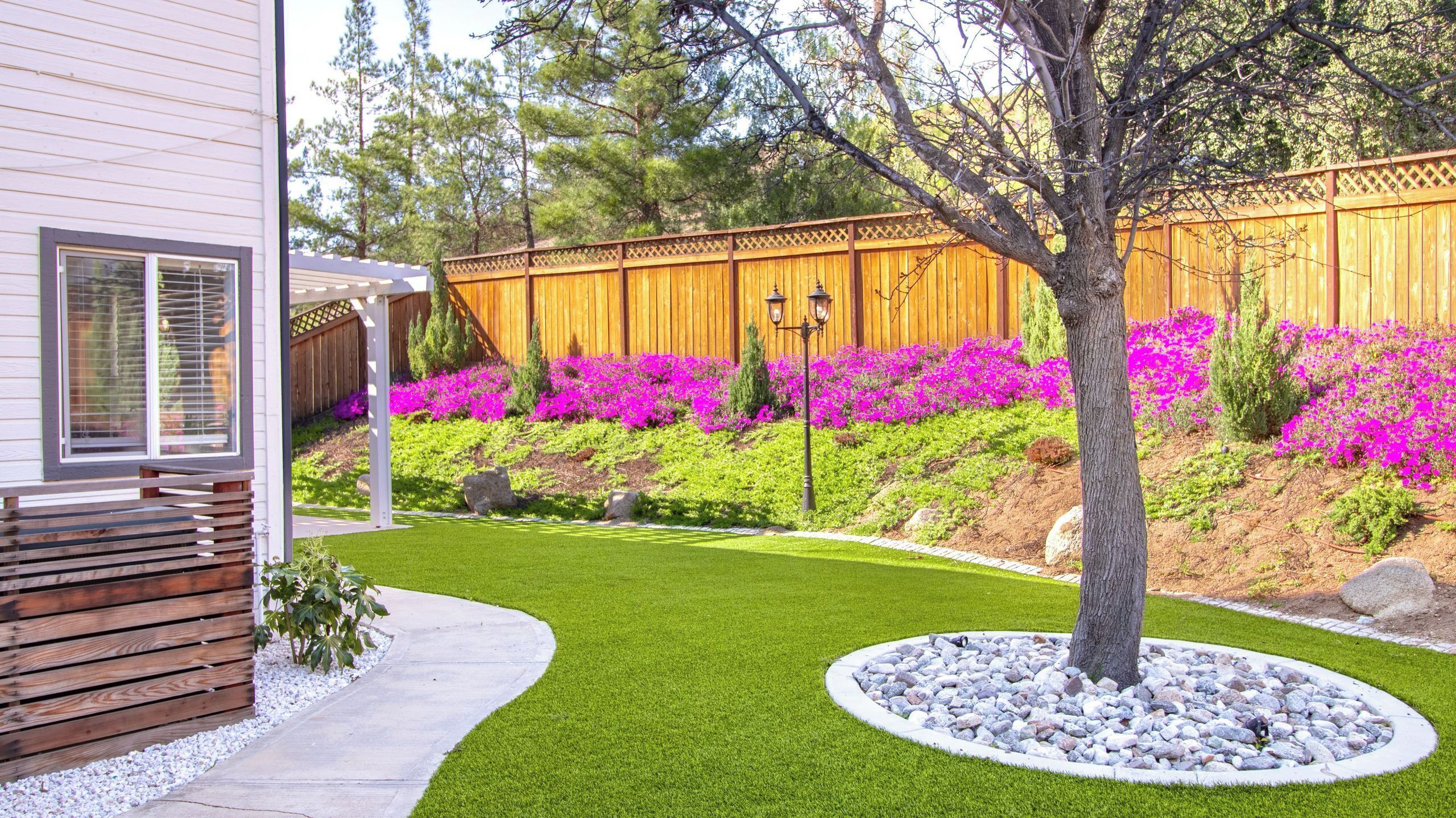 Un jardin bien entretenu, agrémenté d’une clôture en bois, de fleurs aux couleurs vives et d’un arbre au centre.
