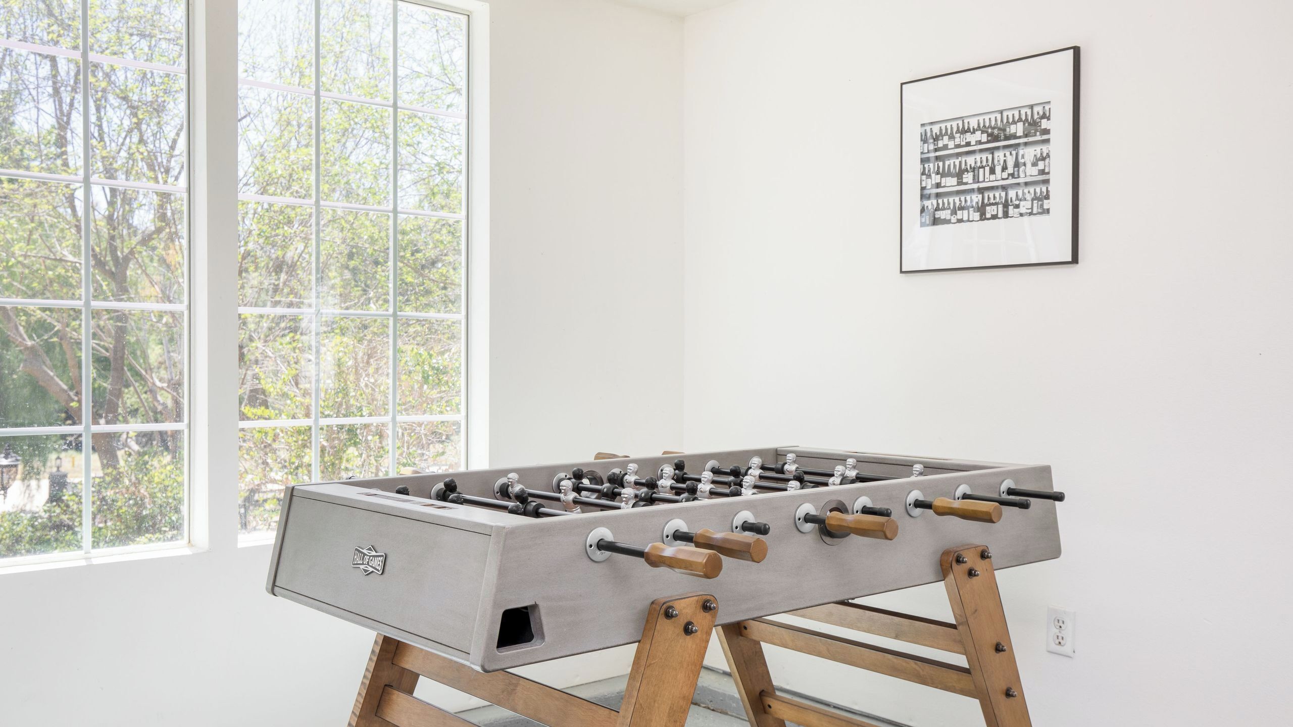 A foosball table in a room with a large window and a framed picture on the wall.