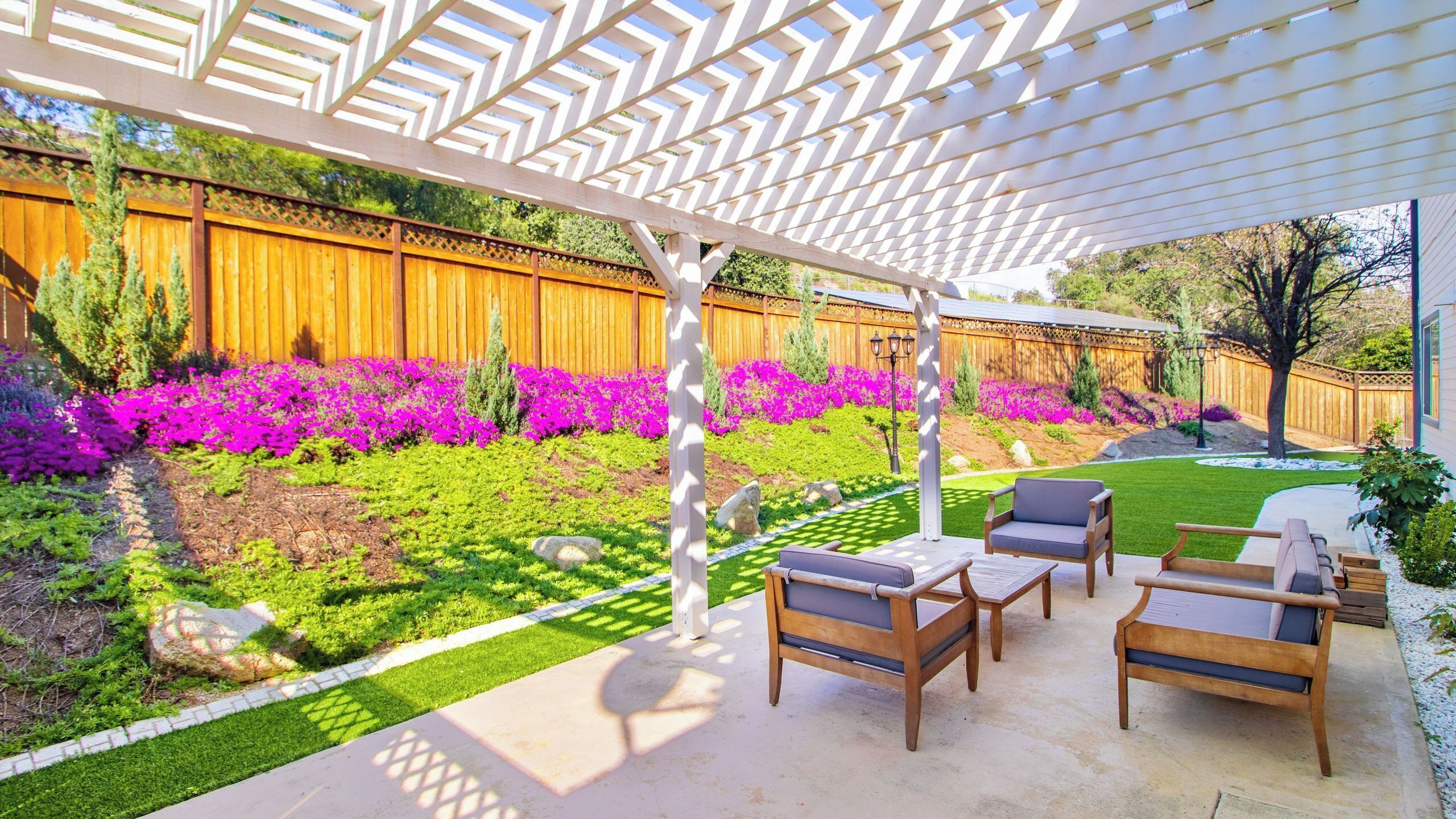 Un patio techado con mobiliario exterior, cerca de madera y coloridos macizos de flores.
