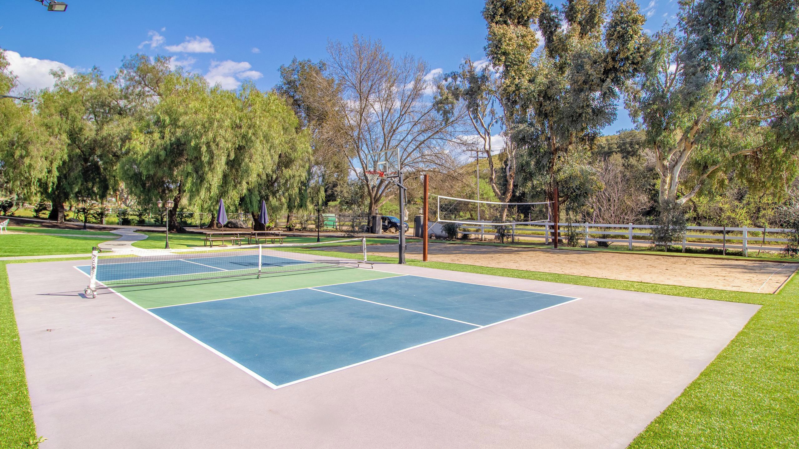 An outdoor tennis court with a net, surrounded by trees and a fence.