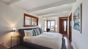 Ein Schlafzimmer mit Bett, Nachttisch, Lampe und einem Fenster mit Jalousien.