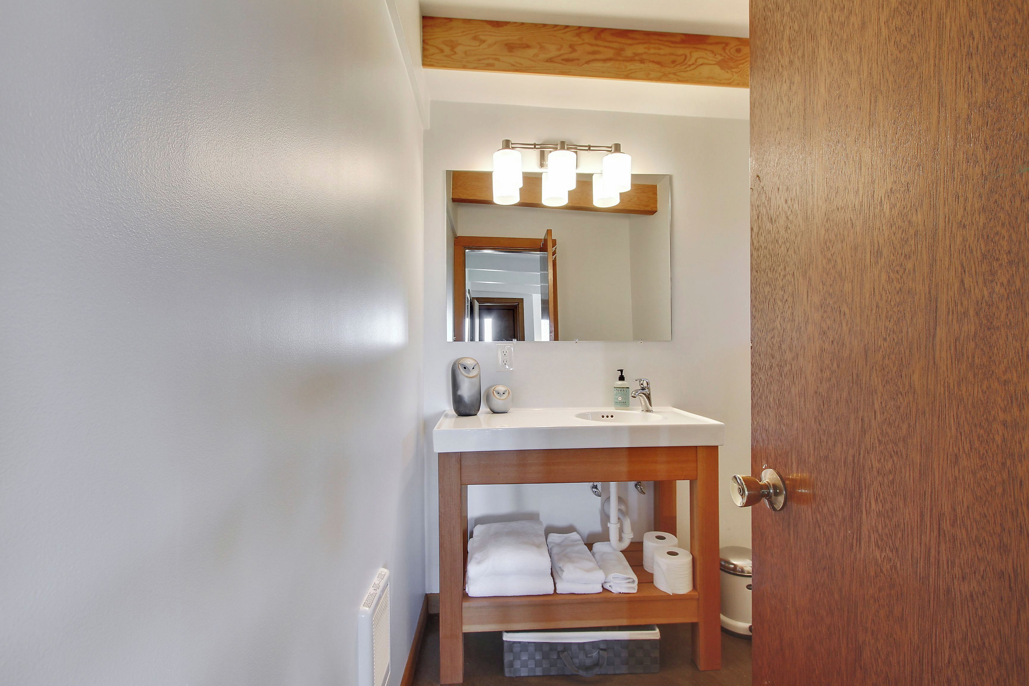 Un baño con tocador de madera, espejo, lavamanos y toallero.