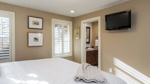 A bedroom with a bed, a television mounted on the wall, and framed pictures on the wall.