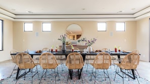 A dining room with a long table, wicker chairs, and a patterned rug. - Luxe Scottsdale Desert Oasis Infinity Pool, Spa, Panoramic Views + Firepit (Cave Creek)