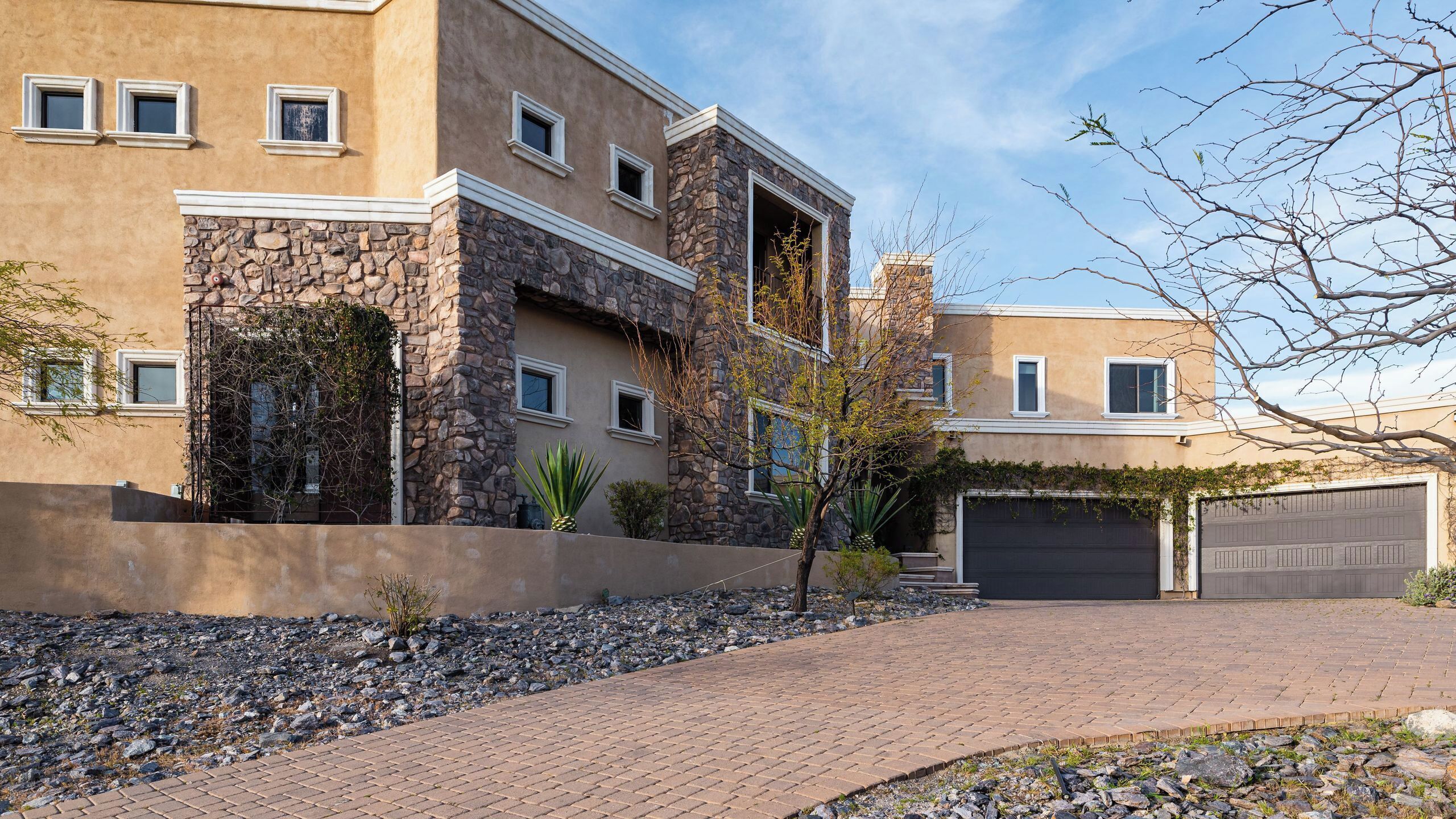 A multi-story residential building with a stone facade, multiple windows, and a paved driveway leading to a garage.