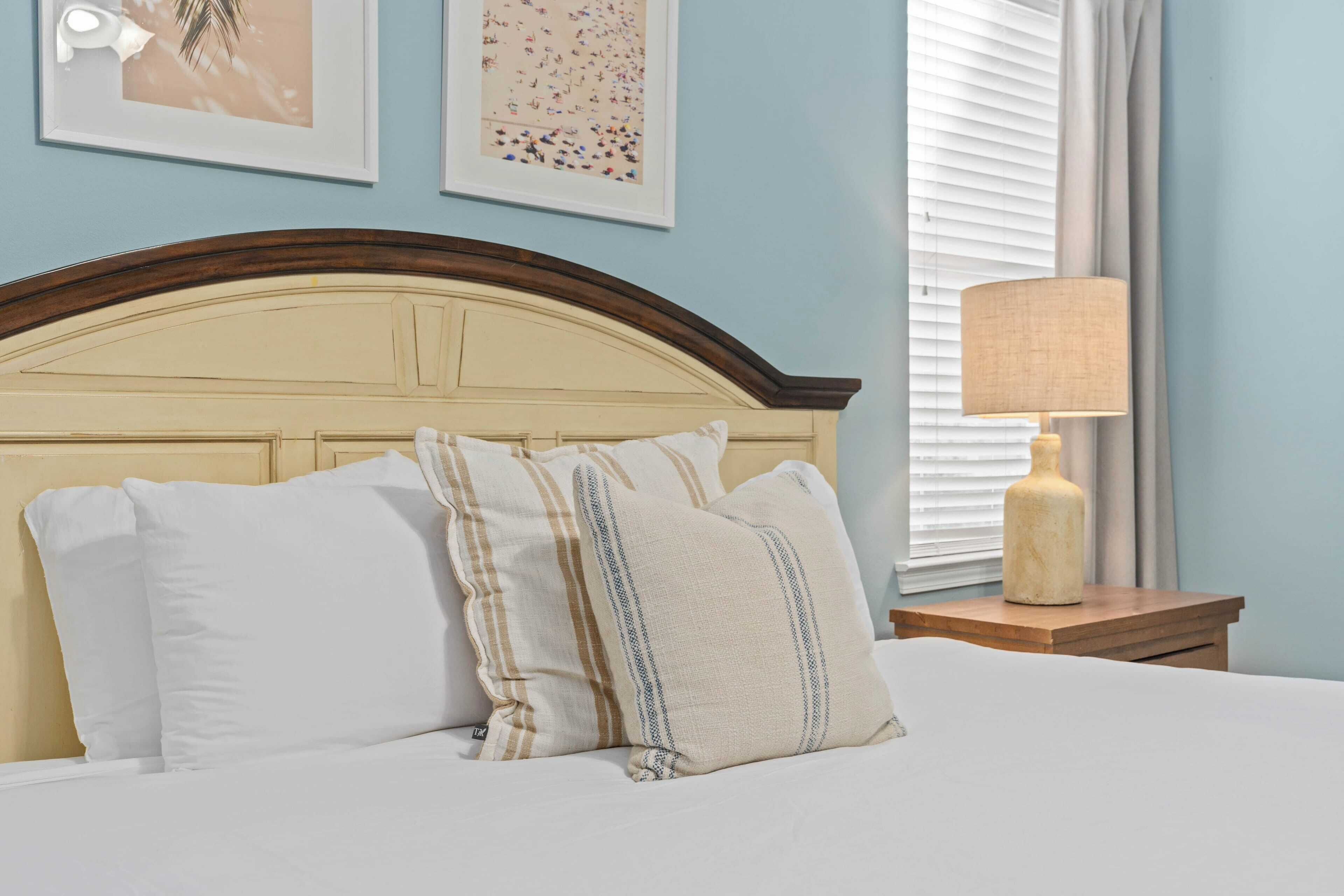 A bed with white and striped pillows, a wooden headboard, and a bedside table with a lamp.