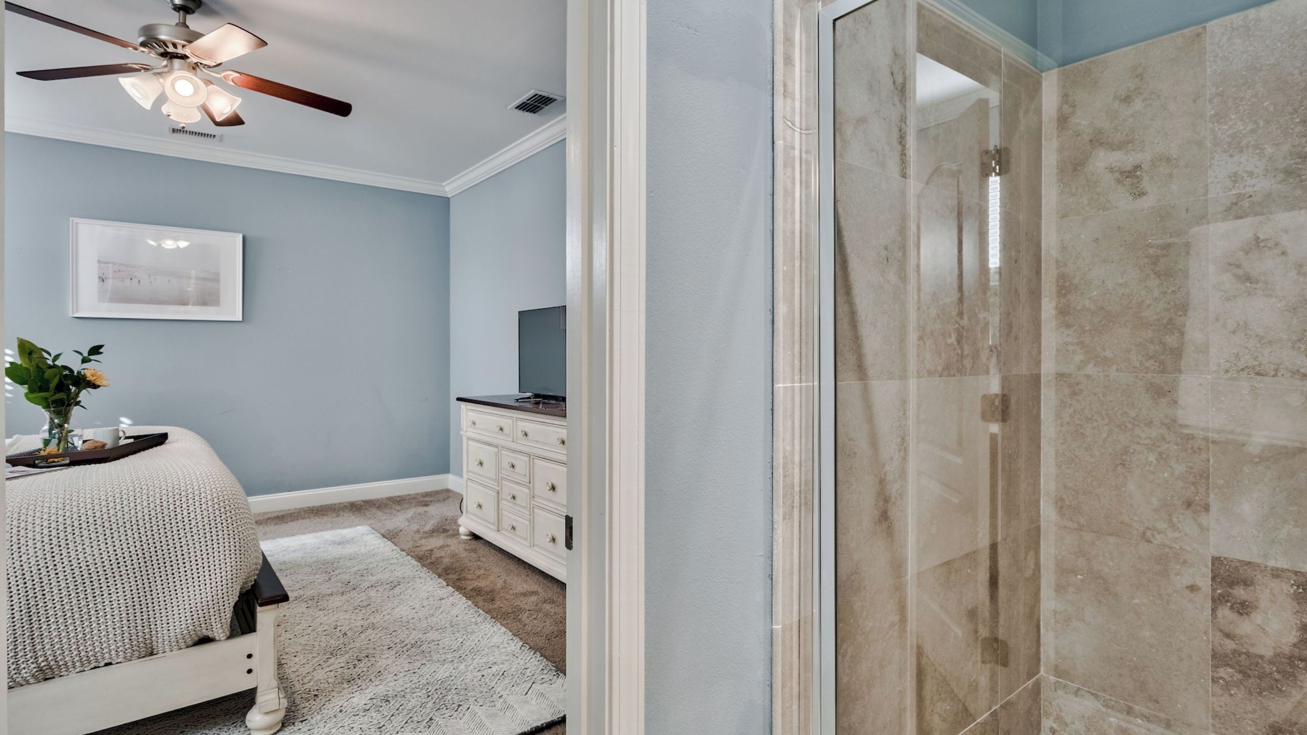 Een slaapkamer met een bed, een dressoir, een plafondventilator en een douche met glazen deur.