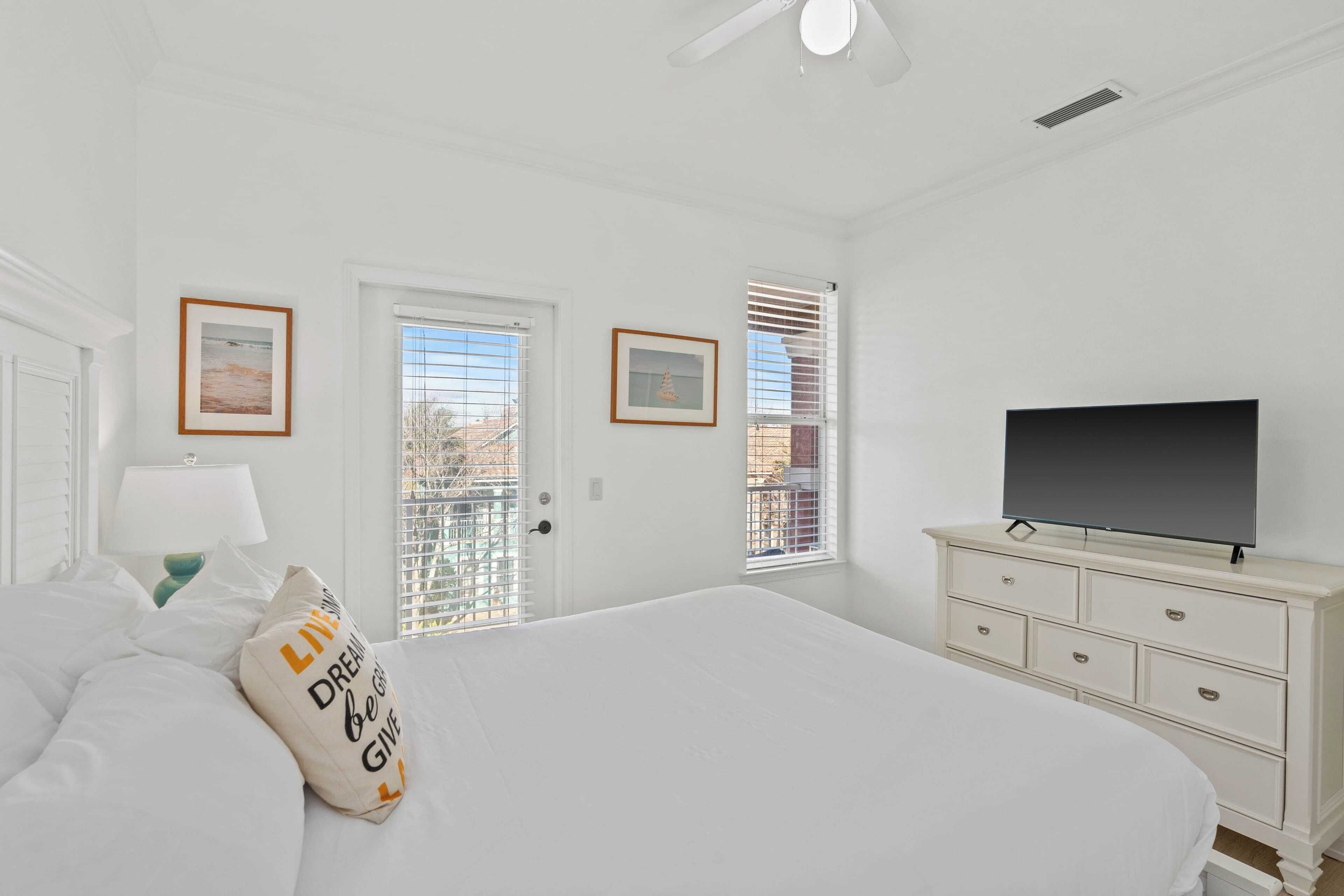 A bedroom with a bed, a dresser, a television, and two windows with blinds.