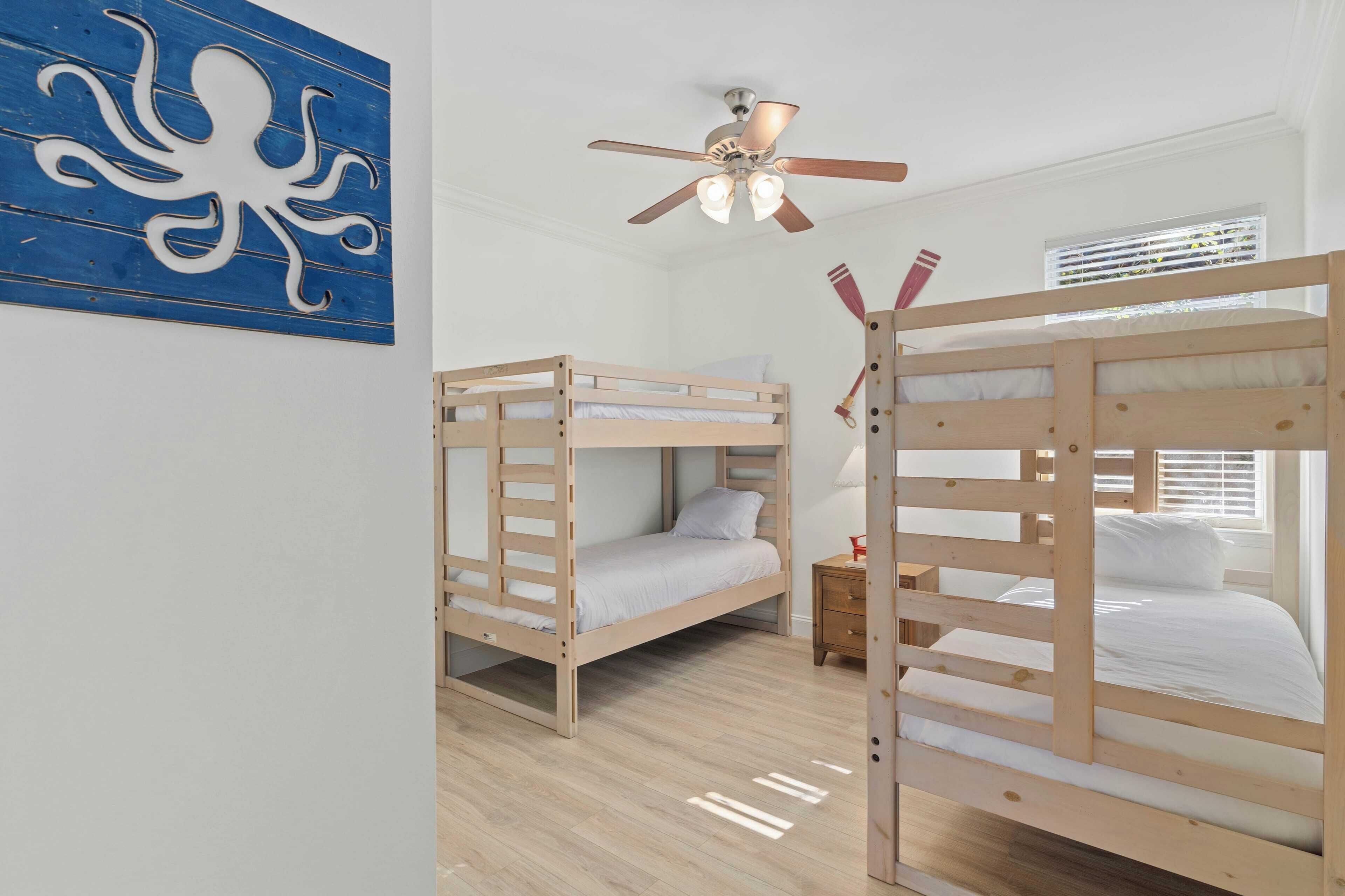 A room with two bunk beds, a ceiling fan, a wooden floor, and a wall with a blue octopus artwork.