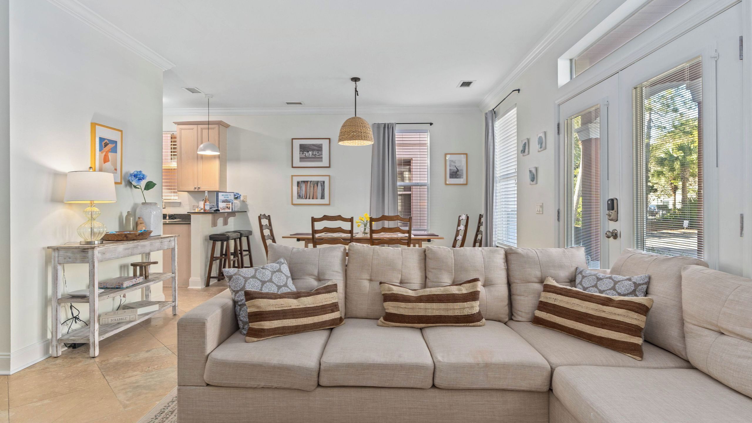 A living room with a sofa, a dining table, chairs, a kitchen area, and a hanging light fixture.