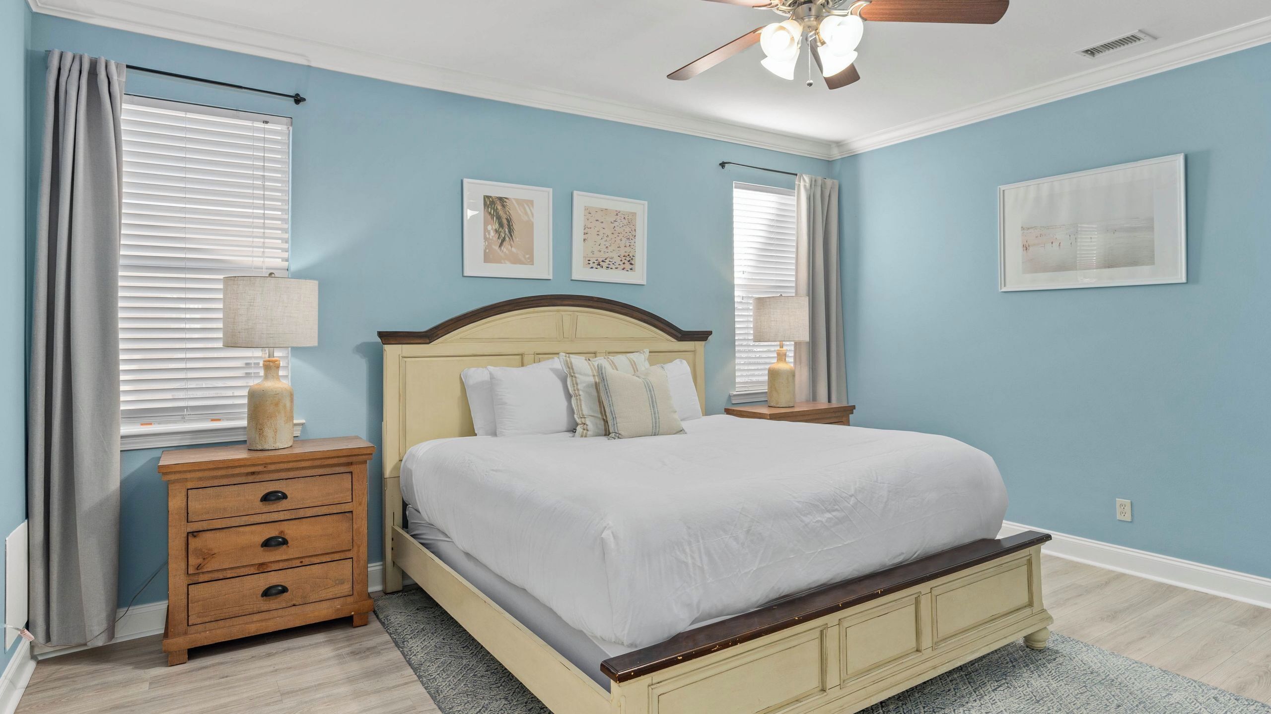 A bedroom with a bed, nightstands, a ceiling fan, and artwork on the walls.